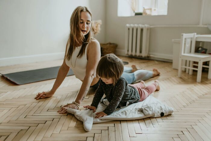 Woman and child stretching on wooden floor in a bright room showing relatable middle class family lifestyle flags