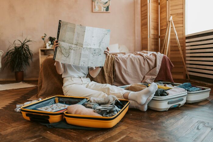 Person sitting on floor packing suitcases and reading a map, preparing for travel to avoid TSA security line delays. Person sitting on floor packing suitcases and reading a map, preparing for travel to avoid TSA security line delays.
