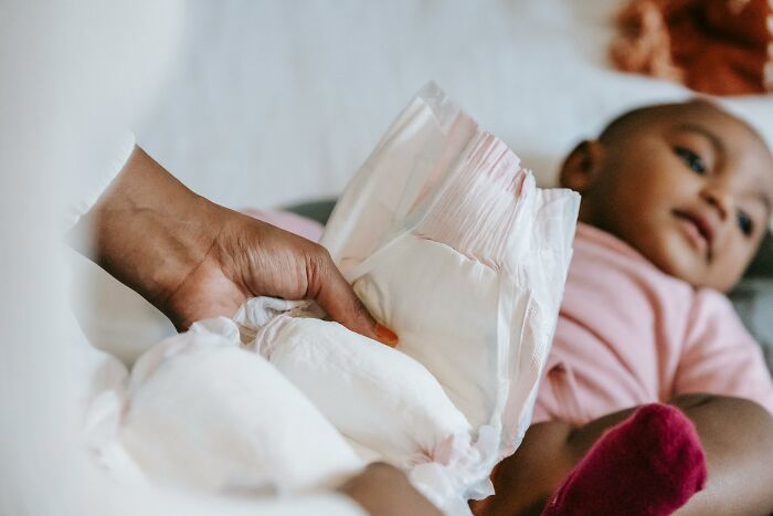 Hand holding diapers near a baby lying down, illustrating people share most privileged things said about caregiving.