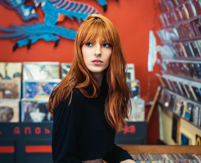 Young woman with red hair and nose ring in a record store, reflecting on dates that went sour and safe word use.