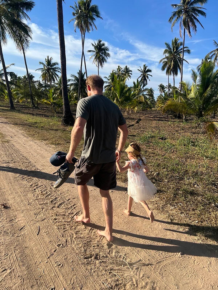 Man and little girl walking barefoot on a dirt path lined with palm trees, sunlight casting long shadows at sunset. Man and little girl walking barefoot on a dirt path lined with palm trees, sunlight casting long shadows at sunset.