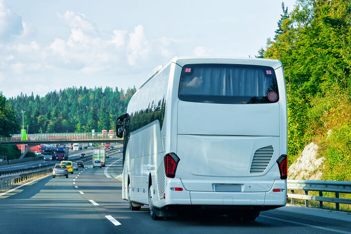 White luxury coach bus driving on highway surrounded by forest, illustrating rich kid meltdowns at private schools.