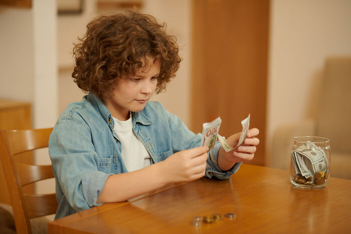 Young boy counting cash at a wooden table, illustrating rich kid meltdowns at private schools.