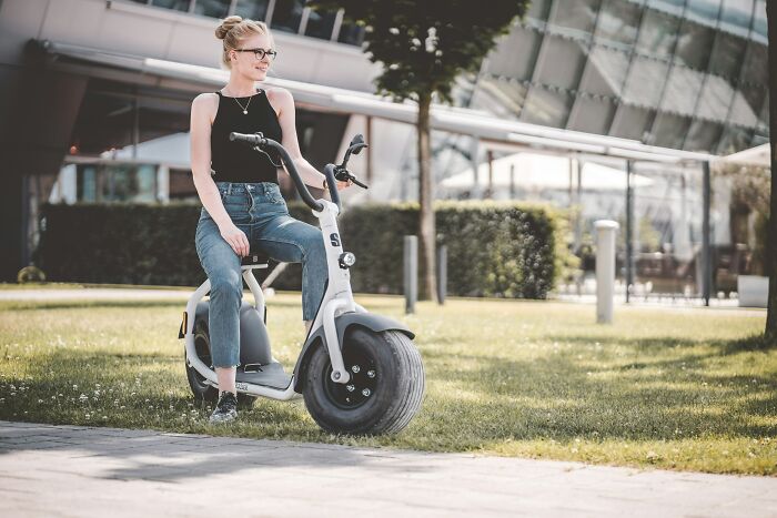 Young woman sitting on electric scooter outside a modern building, illustrating rich kid meltdowns at private schools.