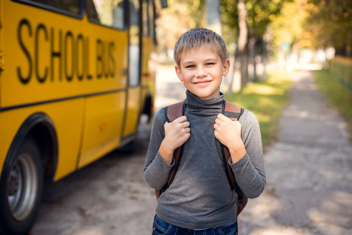 Young student with backpack standing near a yellow school bus, representing rich kid meltdowns at private schools.
