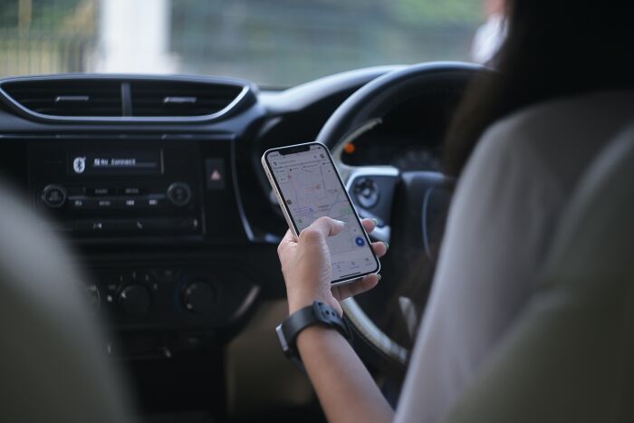 Person using a smartphone with a map app inside a car, illustrating the good trend slowly disappeared in navigation habits.