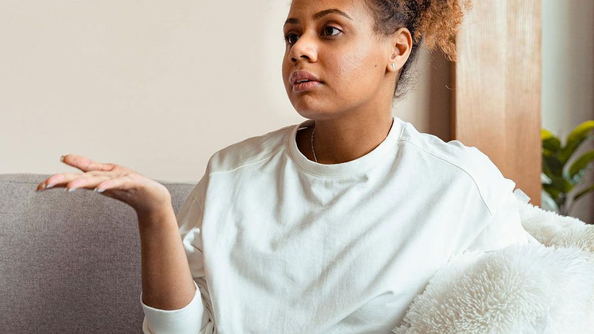 Woman showing subtle red flags, sitting on sofa with a thoughtful and uncertain expression, indoors at home.