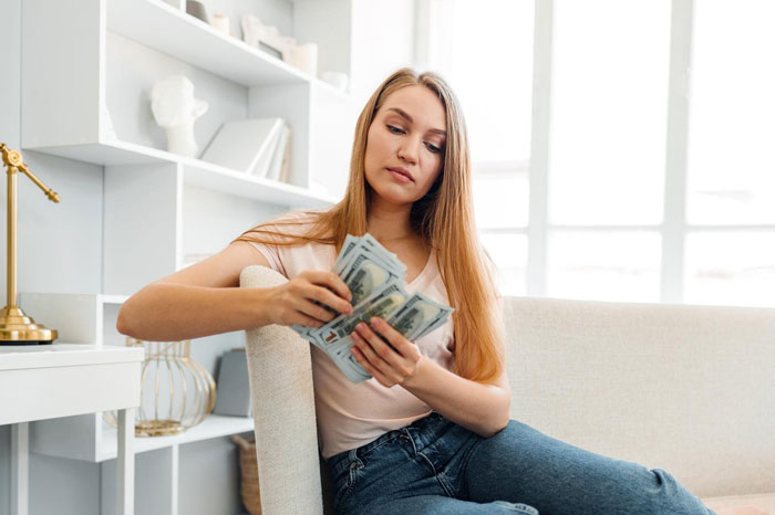 Young woman counting cash at home, representing jobless guy and provider girlfriend financial conflict over money. Young woman counting cash at home, representing jobless guy and provider girlfriend financial conflict over money.