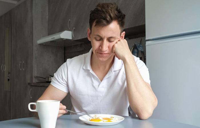 Young man refusing to eat vegan meal looking disappointed at breakfast on girlfriend's birthday in a modern kitchen.