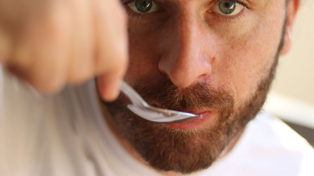 Close-up of a man with beard tasting food with a spoon, representing roommate calls woman stingy over homemade meals.