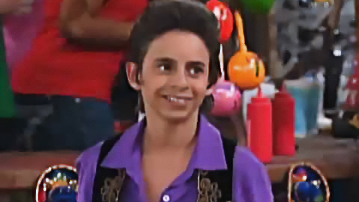 Beloved character from Hannah Montana smiling indoors wearing a purple shirt with ketchup bottles in the background.