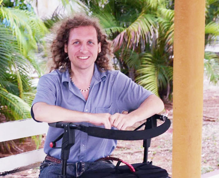 Man trapped in hospital for 9 years sitting outdoors, smiling and leaning on a walker with tropical plants in the background Man trapped in hospital for 9 years sitting outdoors, smiling and leaning on a walker with tropical plants in the background