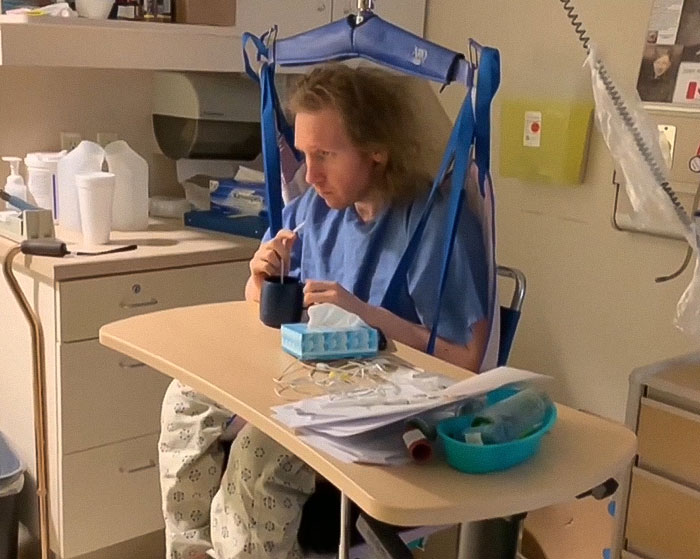 Man trapped in hospital for 9 years sitting at a table in medical gown with hospital equipment around him. Man trapped in hospital for 9 years sitting at a table in medical gown with hospital equipment around him.