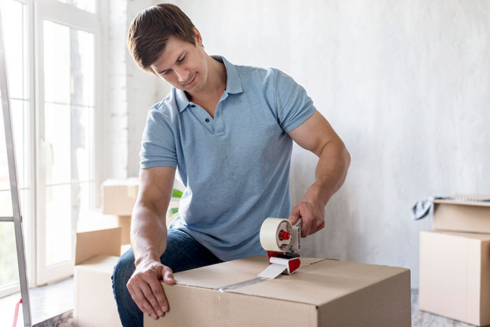 Man packing cardboard boxes indoors, symbolizing a couple kicking out a roomie after kids caused damage despite requests. Man packing cardboard boxes indoors, symbolizing a couple kicking out a roomie after kids caused damage despite requests.