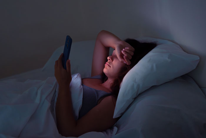 Woman in bed using smartphone at night, tired and restless during nightly gaming marathons, sleep deprivation evident. Woman in bed using smartphone at night, tired and restless during nightly gaming marathons, sleep deprivation evident.