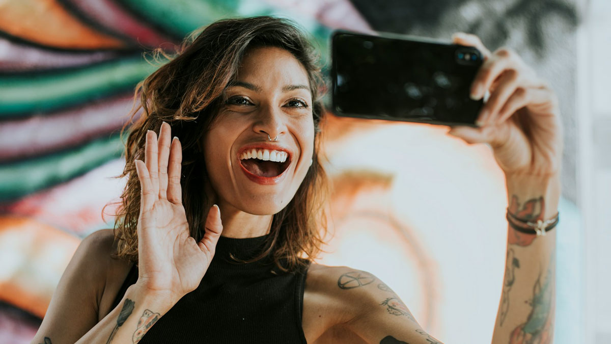Young woman with tattoos smiling and taking a selfie, illustrating behaviors that may indicate someone is insecure.