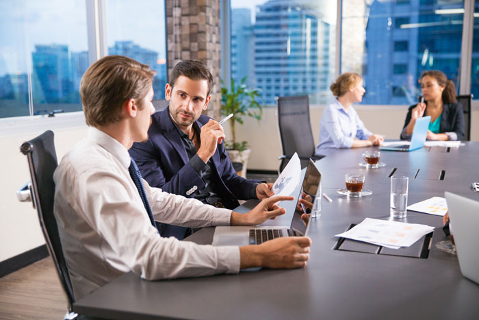Two men discussing bug reports and exploratory testing in a modern office with city views and laptops on the table.