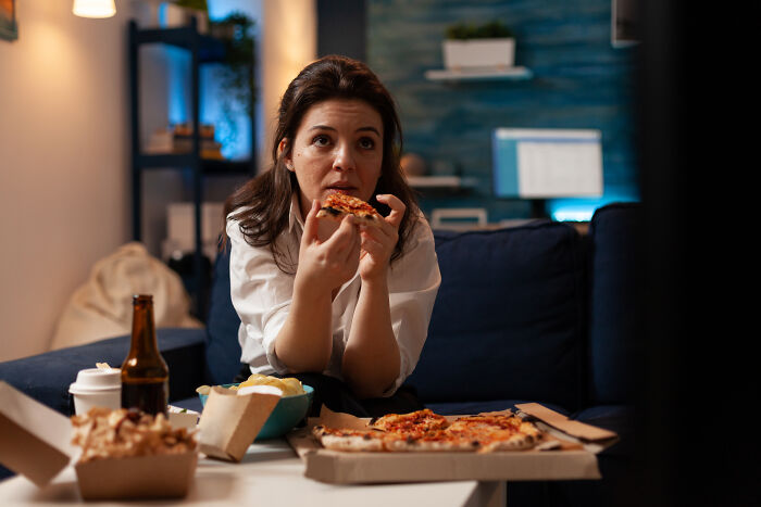 Woman eating pizza alone at home, showing raw and emotional feelings while carrying heavy secrets for years.