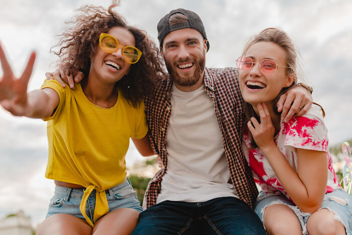 Three friends smiling and embracing outdoors, capturing raw and emotional confessions in a candid moment of connection.