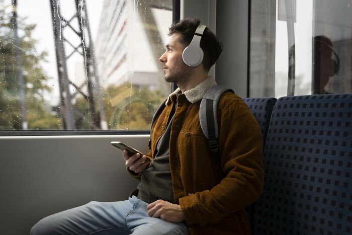 Young man with headphones and phone, sitting alone on a train, reflecting on heavy secrets and emotional confessions.