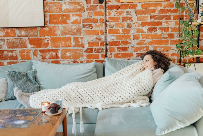 Woman wrapped in a blanket on a couch, symbolizing raw and emotional confessions of carrying heavy secrets.