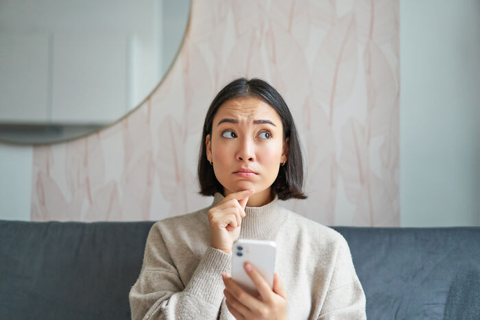 Young woman holding a phone, looking thoughtful and emotional, reflecting on raw confessions and heavy secrets.