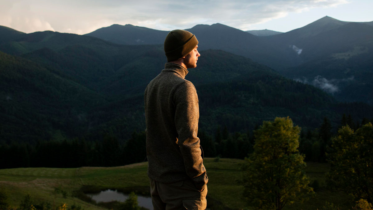 Man wearing a beanie standing alone in nature, reflecting on raw and emotional confessions and heavy secrets.