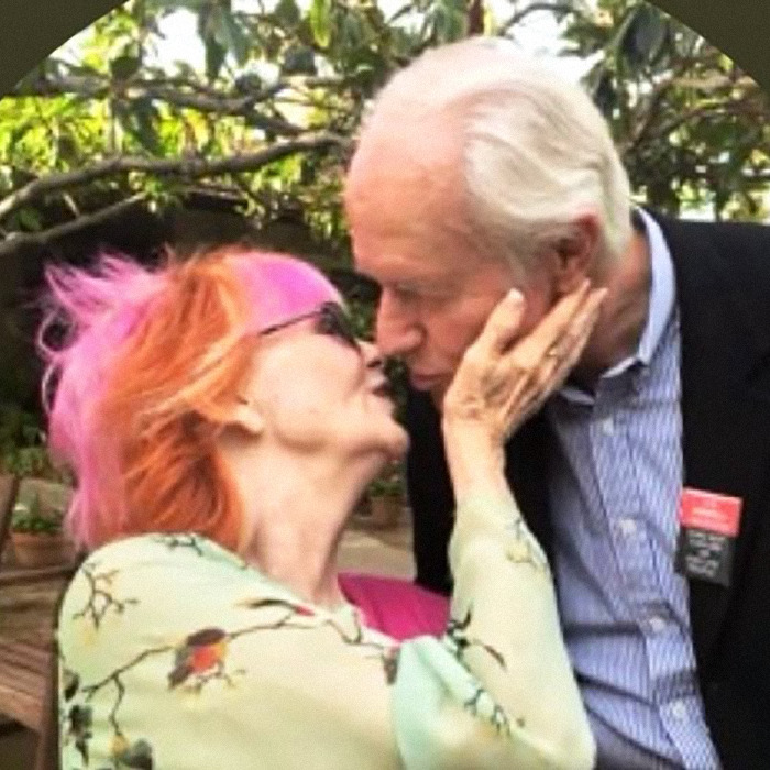 Elderly iconic sitcom legend with bright hair and glasses shares a tender moment during rare public outing. Elderly iconic sitcom legend with bright hair and glasses shares a tender moment during rare public outing.