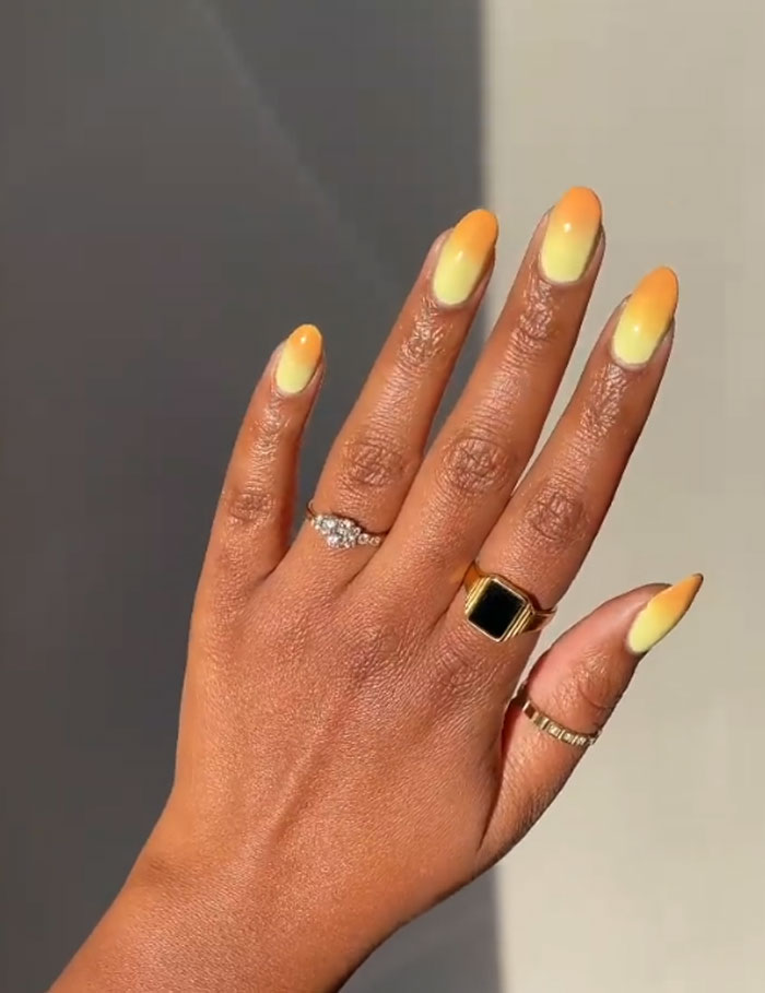 Hand with short French tip nails featuring yellow and orange gradient design, accessorized with gold and silver rings. Hand with short French tip nails featuring yellow and orange gradient design, accessorized with gold and silver rings.