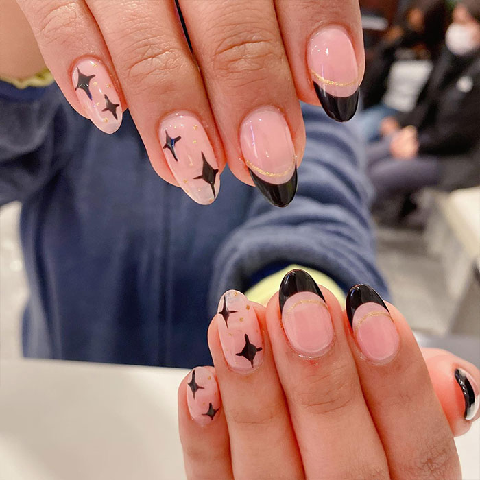 Short French tip nails with black star designs and gold accents on natural nails, showcasing stylish nail art trends. Short French tip nails with black star designs and gold accents on natural nails, showcasing stylish nail art trends.