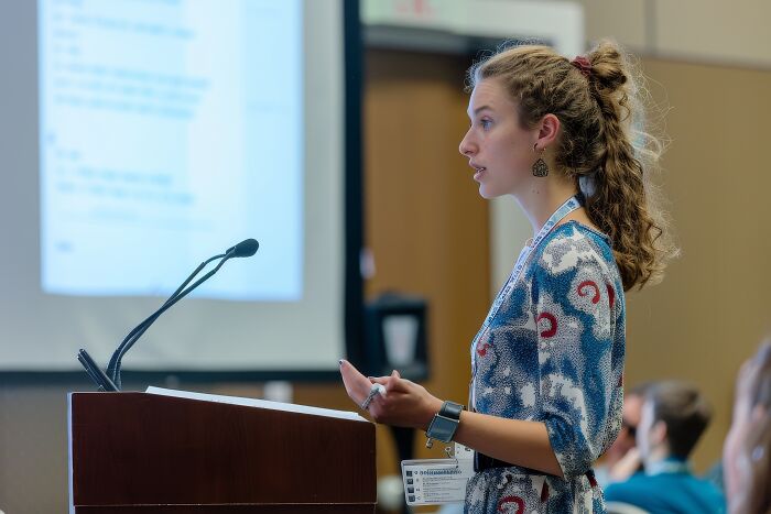 A young woman speaking nervously at a podium, illustrating the challenges of being shy in public situations.