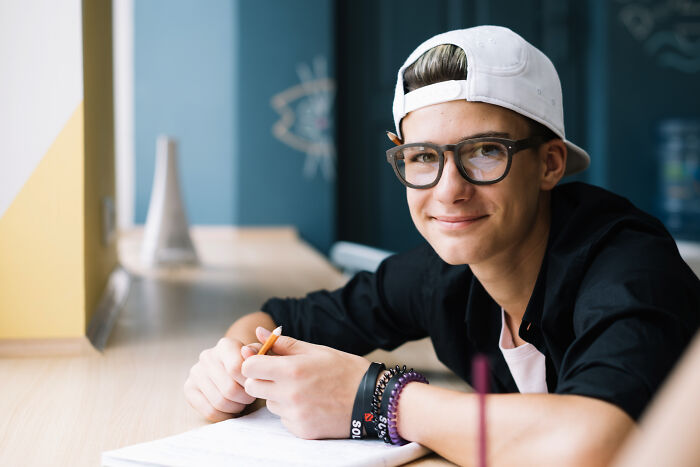 Teen boy wearing glasses and a white cap smiling while studying, reflecting experiences of being shy making things worse.