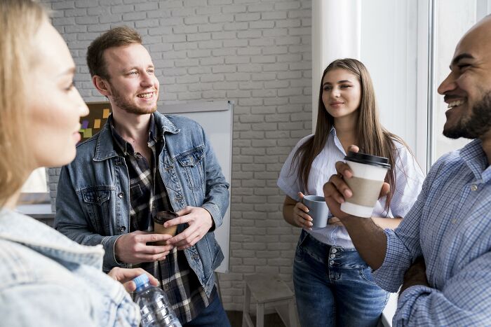Four young adults socializing indoors holding drinks, illustrating challenges of being shy in social situations.
