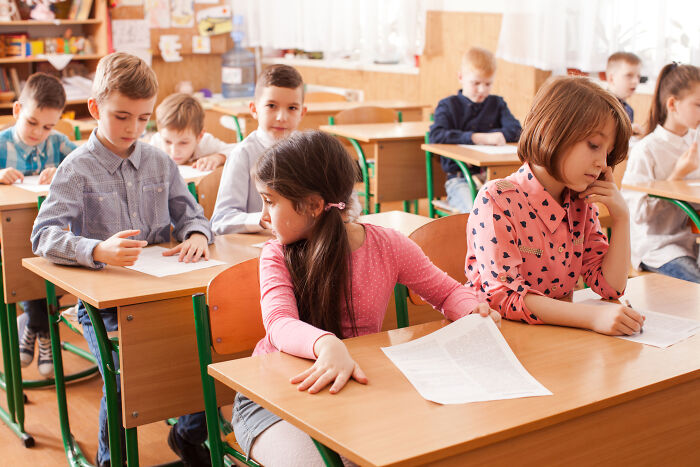 Young students in a classroom showing signs of shyness and discomfort while taking a test or working silently on papers.
