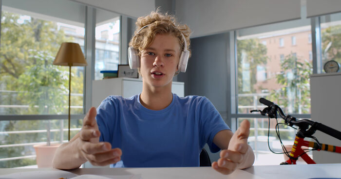 Teen wearing headphones and a blue shirt, speaking with expressive hands in a bright room, illustrating being shy challenges.