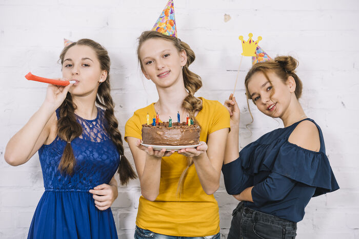 Three shy girls at a birthday party wearing hats, one holding cake, highlighting times being shy made things worse.