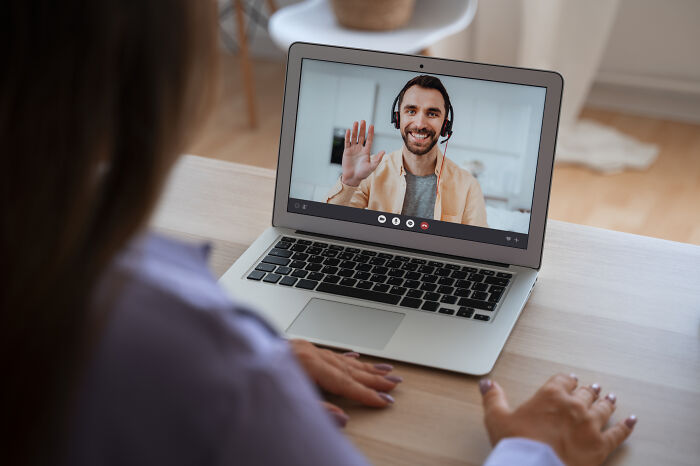 Person on laptop screen wearing headset, waving during a video call, illustrating challenges of being shy in communication.