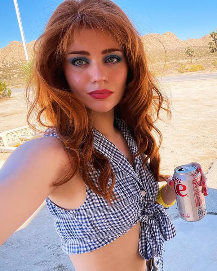 Young woman with red hair and bold makeup holds a soda can outdoors, highlighting child star's unrecognizable transformation. Young woman with red hair and bold makeup holds a soda can outdoors, highlighting child star's unrecognizable transformation.