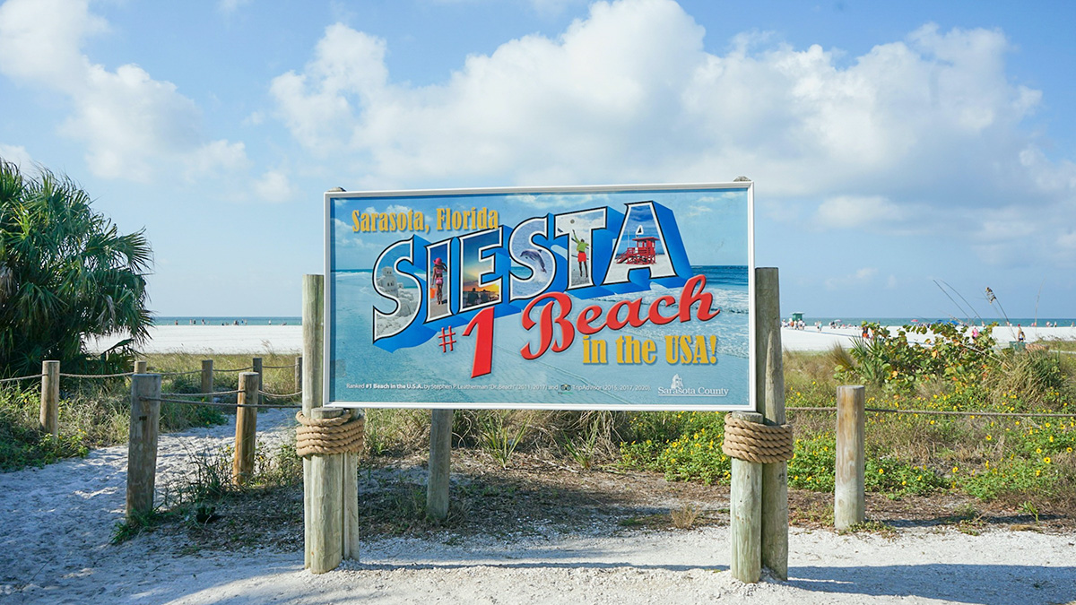 Siesta Key beach sign showing it as the number 1 beach in the US with sand and ocean in the background.