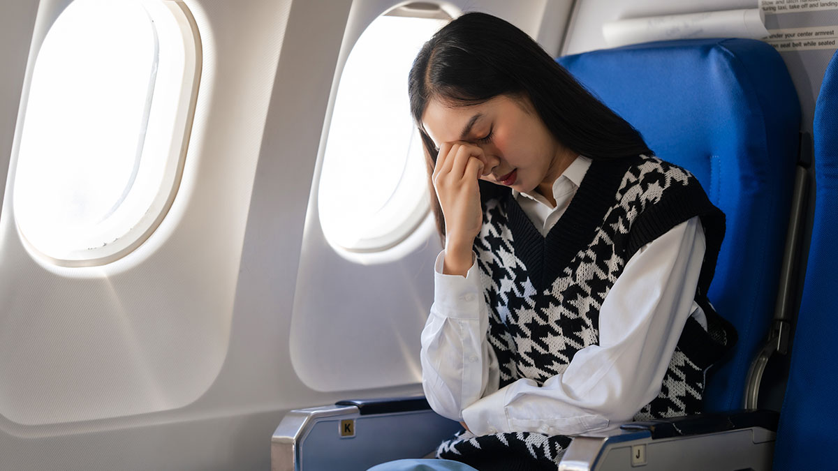 Young woman feeling stressed sitting in airplane seat by window during flight, reflecting on babysit nephew trip.