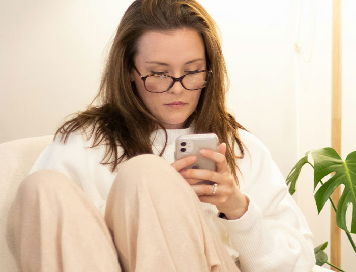 Woman wearing glasses looking upset while using smartphone, reflecting on sister sabotaging birthday dinner plans. Woman wearing glasses looking upset while using smartphone, reflecting on sister sabotaging birthday dinner plans.