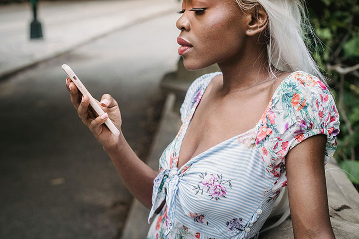 Woman with long blonde hair looking at phone outdoors, reflecting on graduation day ruined by hubby seating issue. Woman with long blonde hair looking at phone outdoors, reflecting on graduation day ruined by hubby seating issue.