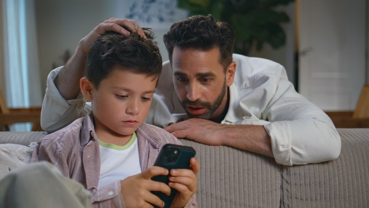 Father watching young boy intensely using smartphone at home, illustrating new iPad kid concept and ChatGPT interaction.