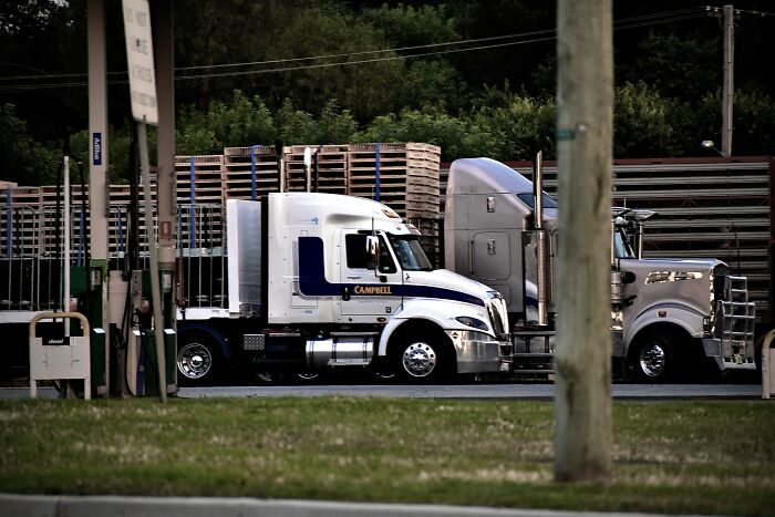 Two large trucks parked at a fuel station, illustrating adults showing they never moved on from their glory days in high school.