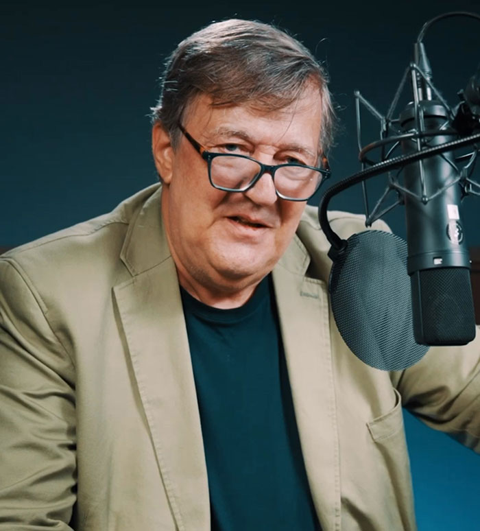 Stephen Fry speaking into a microphone, wearing glasses and a beige jacket, delivering a brutal takedown commentary. Stephen Fry speaking into a microphone, wearing glasses and a beige jacket, delivering a brutal takedown commentary.