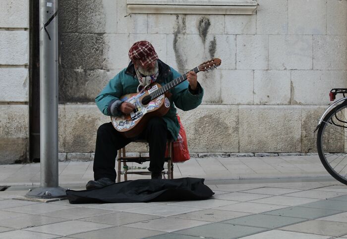 Man wearing a cap playing guitar on a city street, symbolizing priceless reward stories after spending a dollar