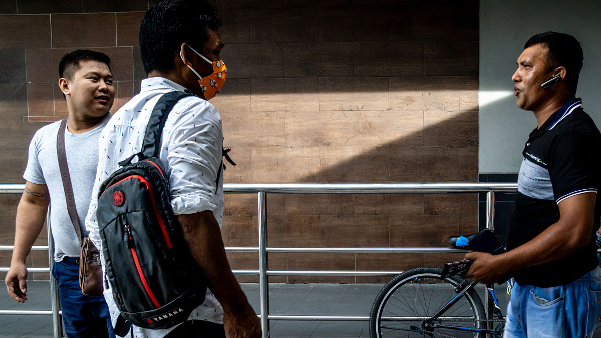 Three men in candid street photo, one wearing a face mask and backpack, capturing the quiet beauty of everyday life outdoors.
