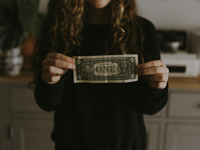 Teen girl holding a dollar bill, showing the struggle of babysitting step siblings and earning money.