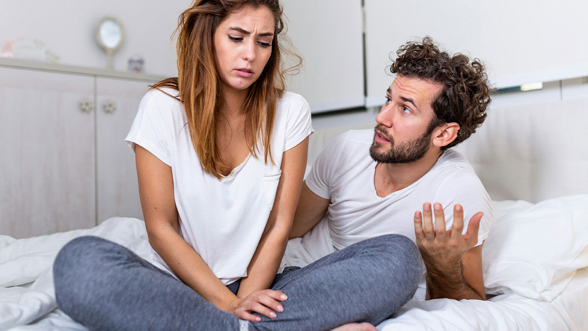 Young couple having tense conversation on bed, illustrating toxic dating trends in relationships and emotional conflict.