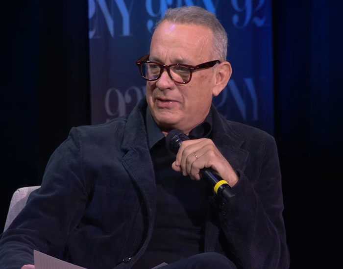 Tom Hanks speaking into a microphone during an interview, addressing childhood confusion violence and deprivation. Tom Hanks speaking into a microphone during an interview, addressing childhood confusion violence and deprivation.